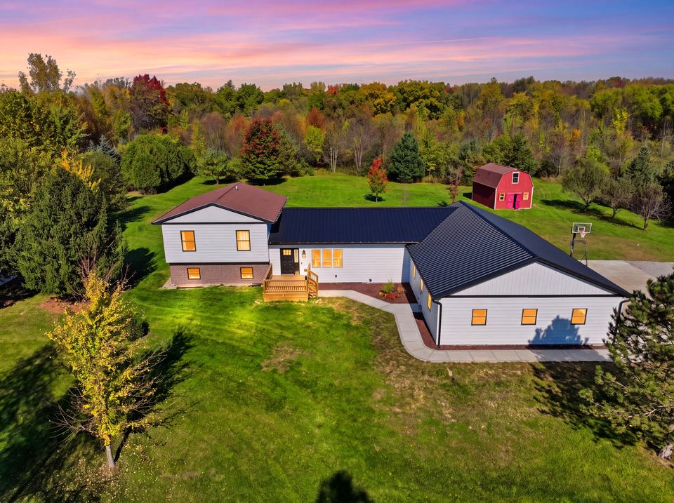 Aerial twilight view of a farmhouse and red barn on a wooded lot